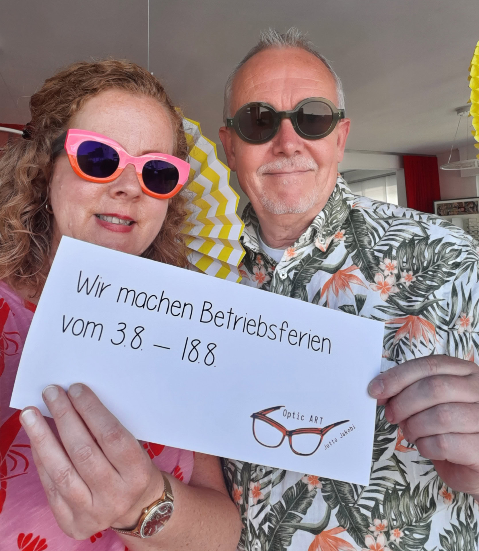Zwei Personen mit Betriebsferien-Schild, bunte Brillen.