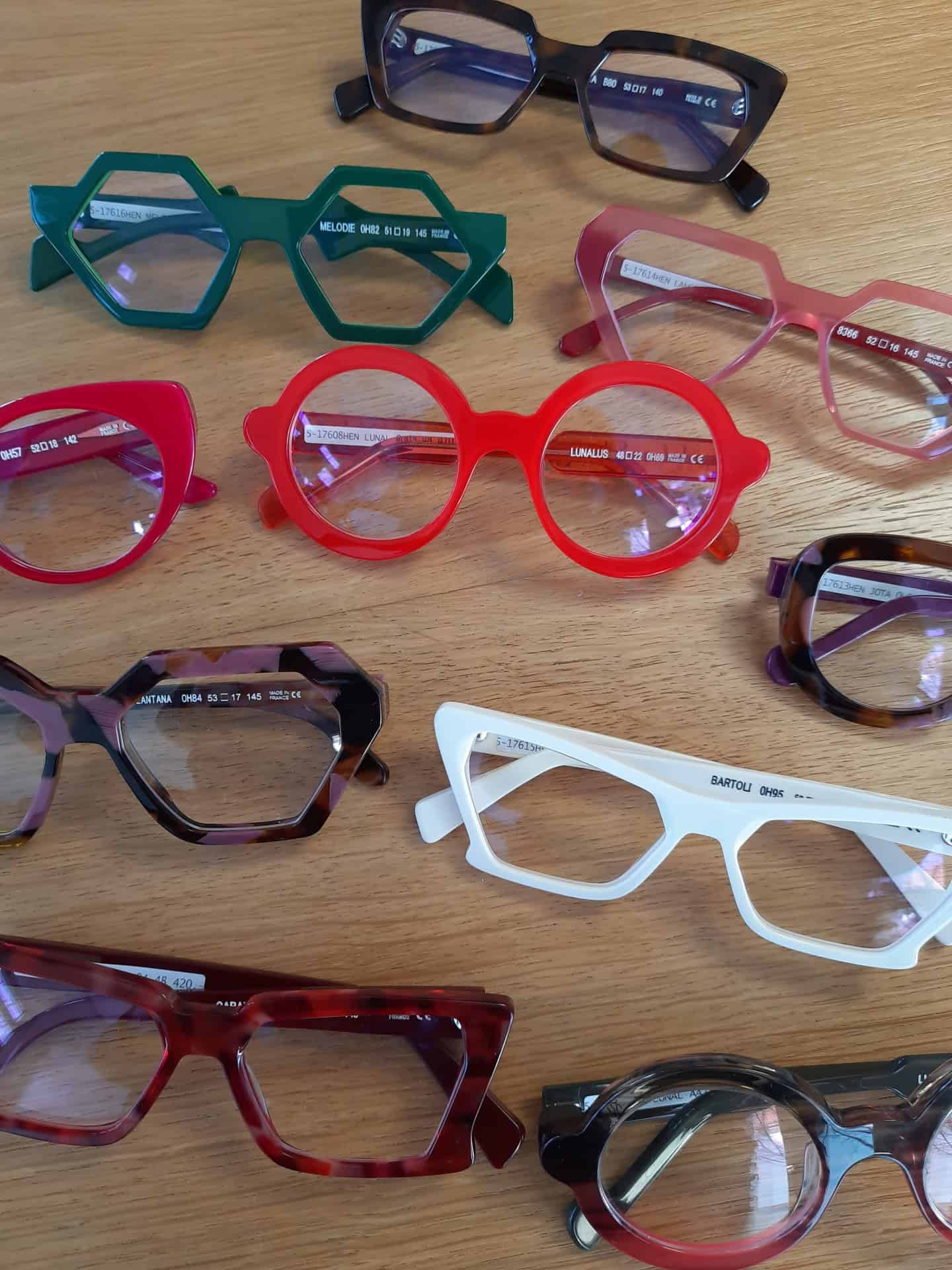 Bunte Brillengestelle auf Holztisch angeordnet.