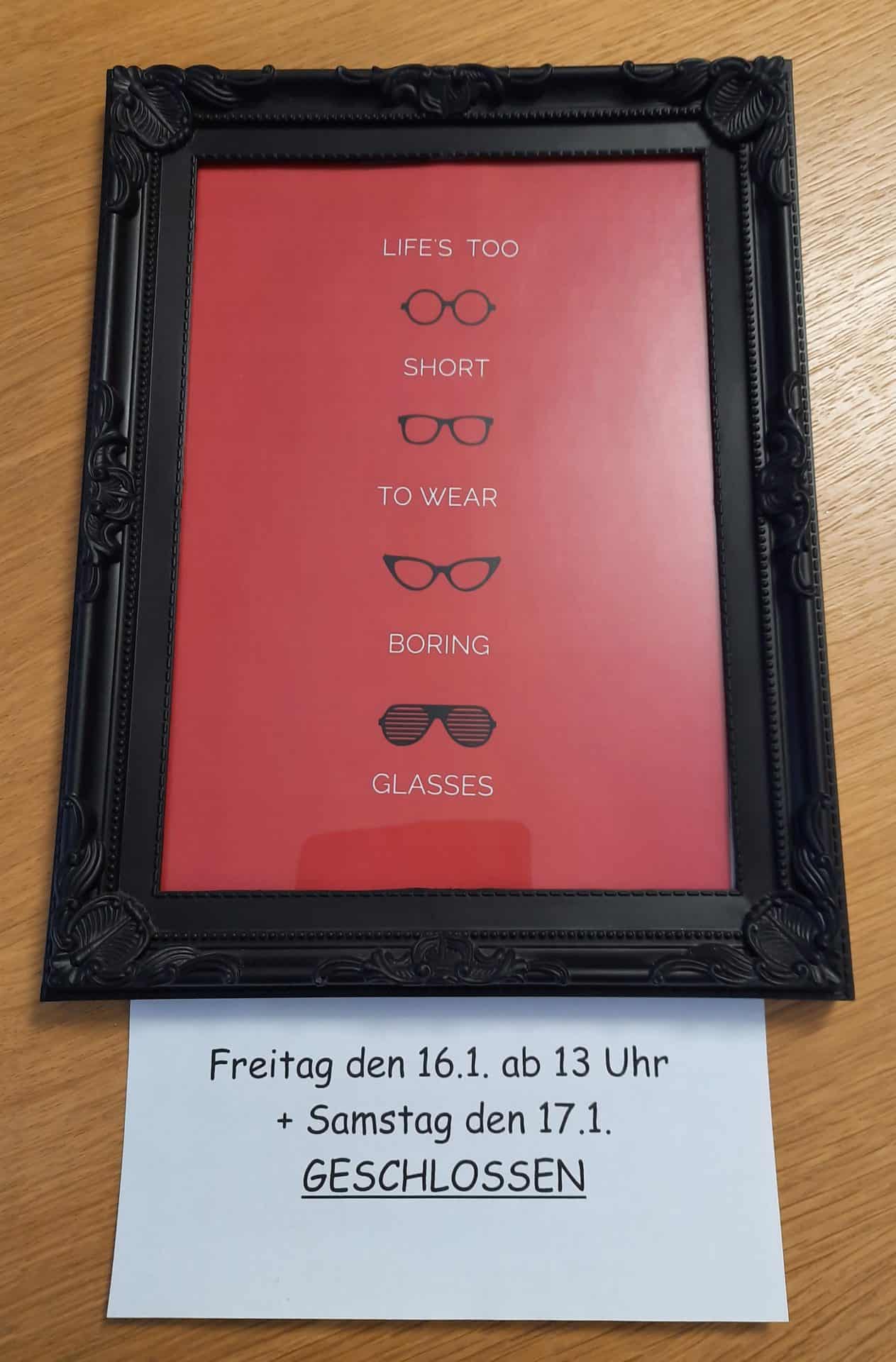 Dekorativ gerahmtes Schild mit Brillenmotiv und Schließzeiten.